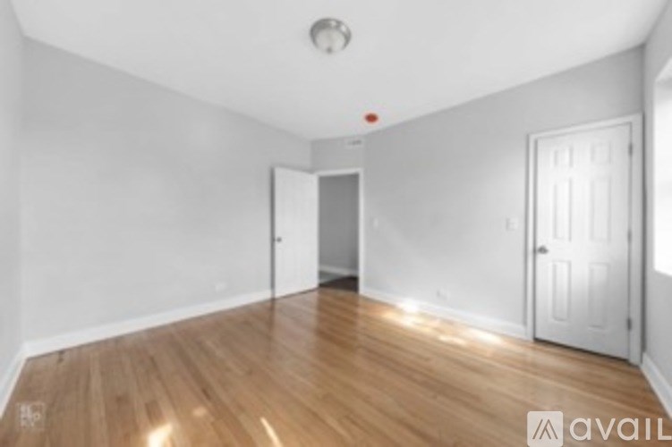 A room with wooden floors and white walls, with a door on the right and a smaller door on the left.