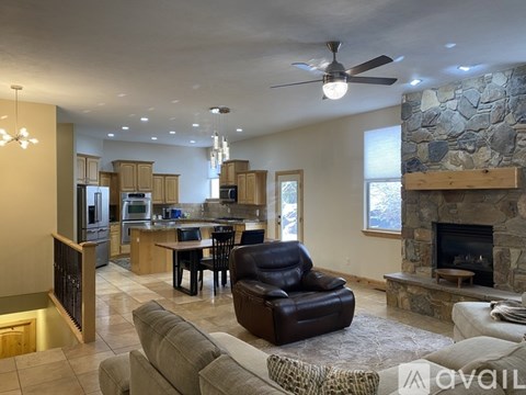 A living room with a stone fireplace and a kitchen area in the background.