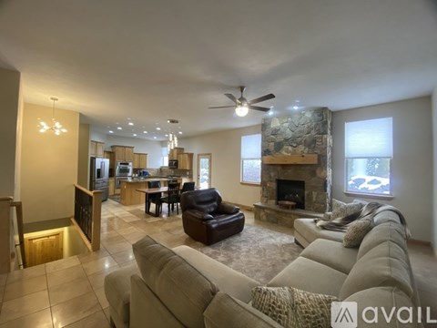 A spacious living room with a stone fireplace and a dining area in the background.