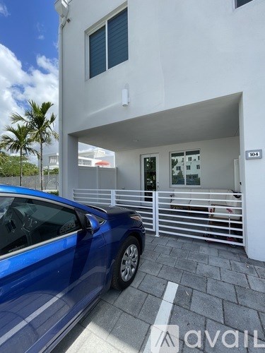 A blue car is parked in front of a white building with a glass door.