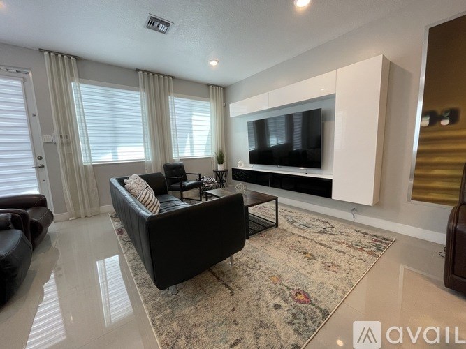 A living room with a black couch and a television mounted on the wall.