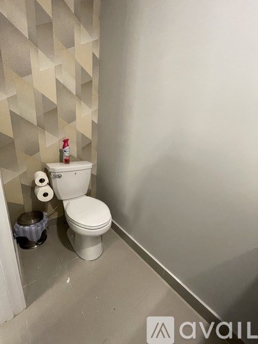 A white toilet with a roll of toilet paper and a bottle of cleaner on top of it.