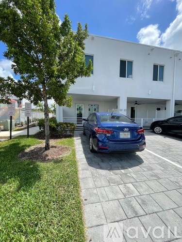A blue car is parked in a parking lot in front of a white building.