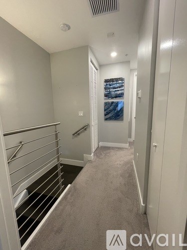 A hallway with a carpeted floor and a metal railing on the left side.