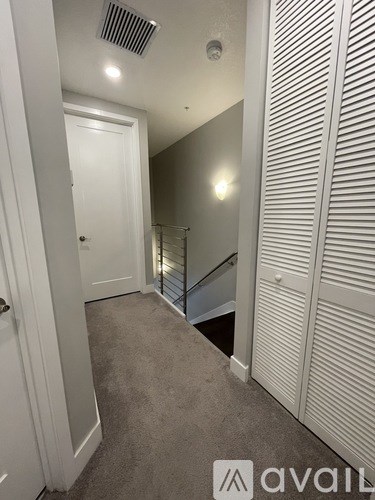 A hallway with a carpeted floor, a white door, and a staircase with a metal railing.
