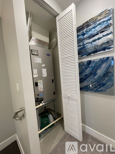 A white door is open to a small room with a fridge and a painting on the wall.