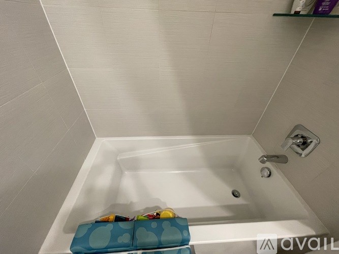 A white bathtub with a blue towel and a bottle of lotion on the side.