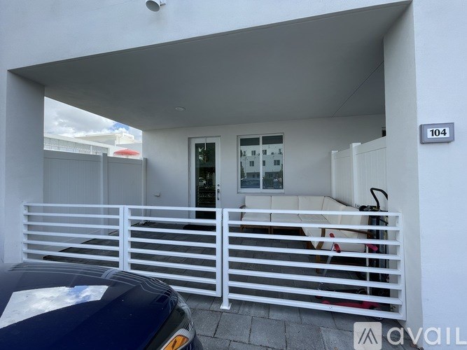 A car is parked in front of a white building with a black car on the left.
