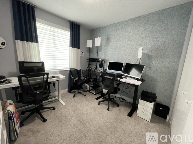 A room with two desks and chairs, one of which is a gaming chair.