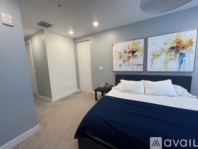 A bedroom with a bed, nightstand, and two paintings on the wall.