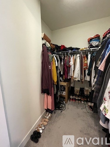 A small closet with clothes hanging and shoes on the floor.