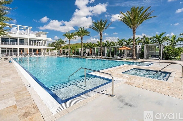 A large outdoor swimming pool surrounded by palm trees and a white building.