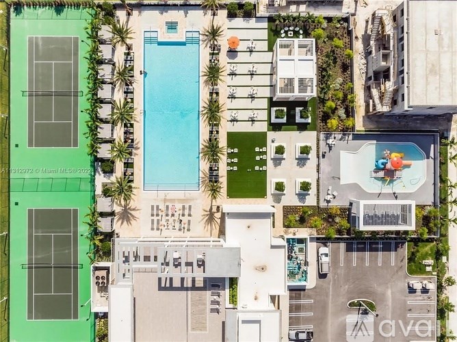 A large swimming pool is surrounded by a green fence and palm trees.