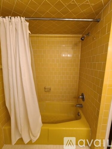 A yellow tiled shower with a white curtain.