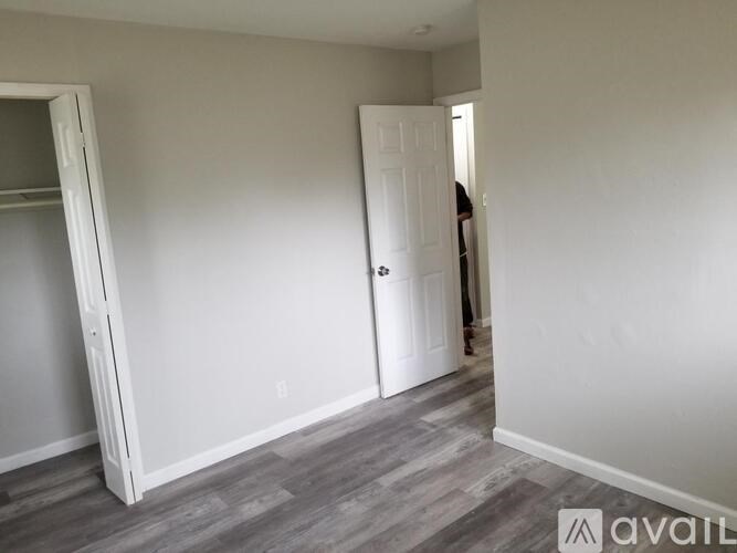 A room with a grey floor and white walls with a door and a person in the background.