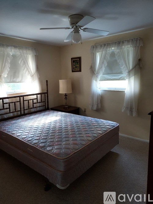 A bedroom with a bed, a ceiling fan, and a window with curtains.