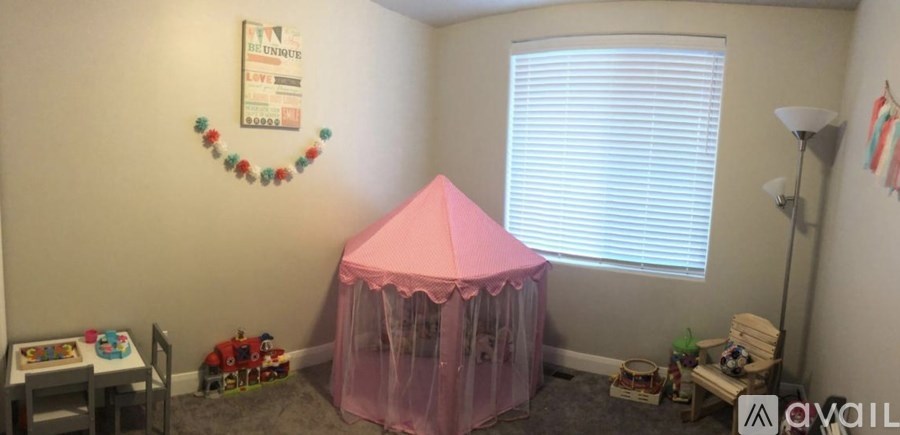 A pink tent is in the corner of a room with a white wall and a window.