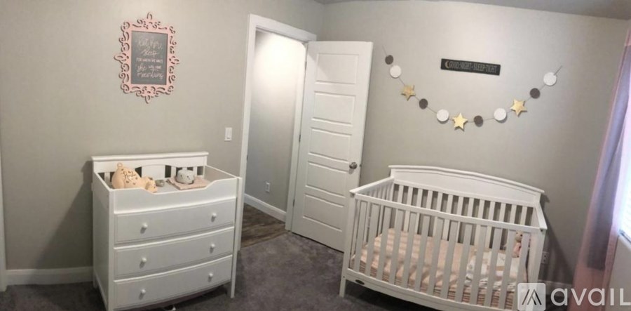 A baby nursery with a white crib and dresser, a teddy bear, and a star-shaped decoration on the wall.