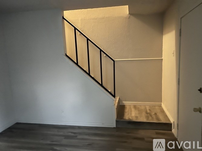 A staircase with a black railing leads up to a landing with a white wall and a door.
