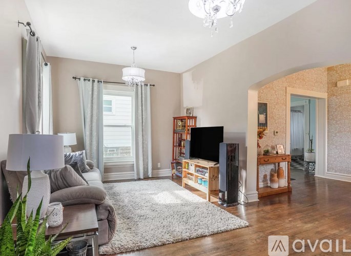 A living room with a grey couch, a white rug, a wooden entertainment center, and a chandelier.