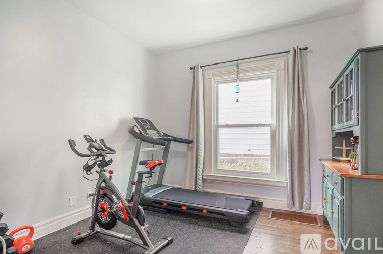A room with a treadmill, exercise bike, and a cabinet.