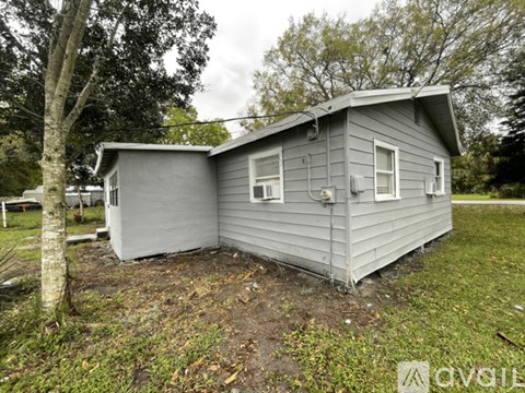 A small grey house with a tree in front of it.