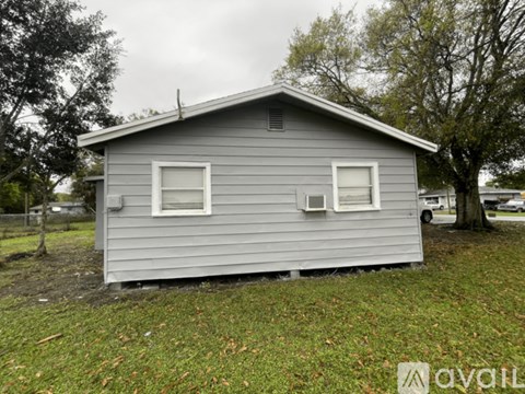 A small grey house with two windows and a door is situated in a grassy area.