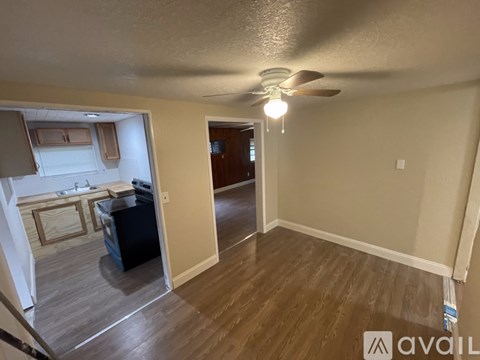 A living room with a ceiling fan and a kitchen area in the background.