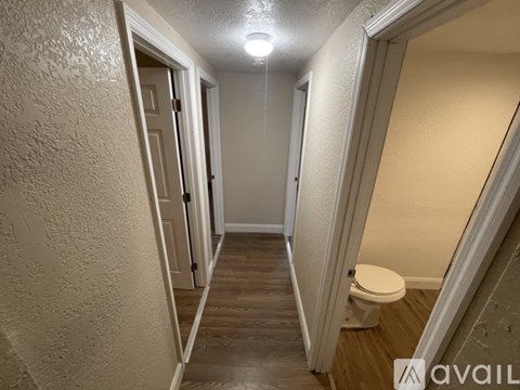 A narrow hallway with a toilet on the right and a door on the left.