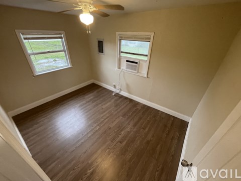 A room with a ceiling fan and two windows.