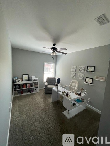 A room with a fan, a chair, and a table with various objects on it.