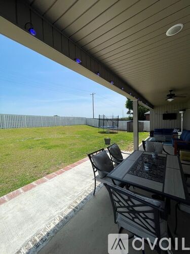 A patio with a table and chairs overlooking a fenced yard.