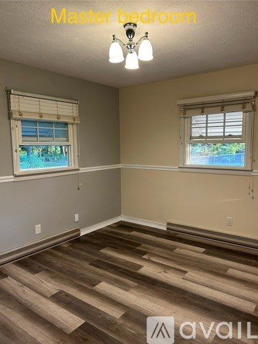 A master bedroom with wood flooring and two windows.