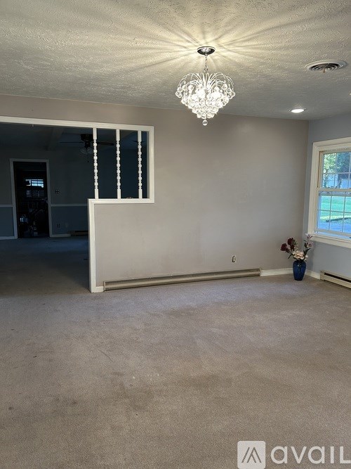 A room with a chandelier, a window with blinds, and a vase with flowers on the windowsill.