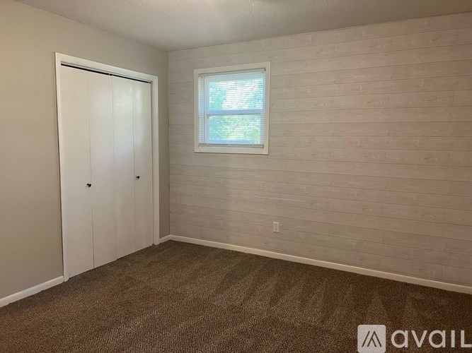 A room with a carpeted floor, a door, and a window with blinds.
