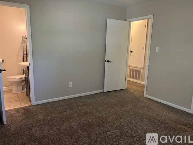 A room with a carpeted floor and a toilet visible through an open door.