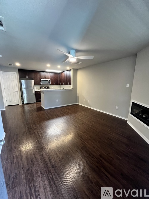 A spacious living room with wood flooring and a kitchen area in the background.