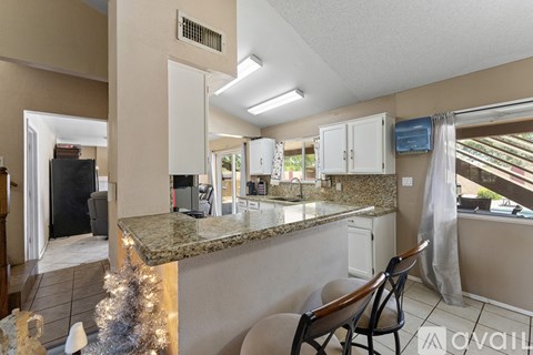A kitchen with granite countertops and a dining area with chairs.