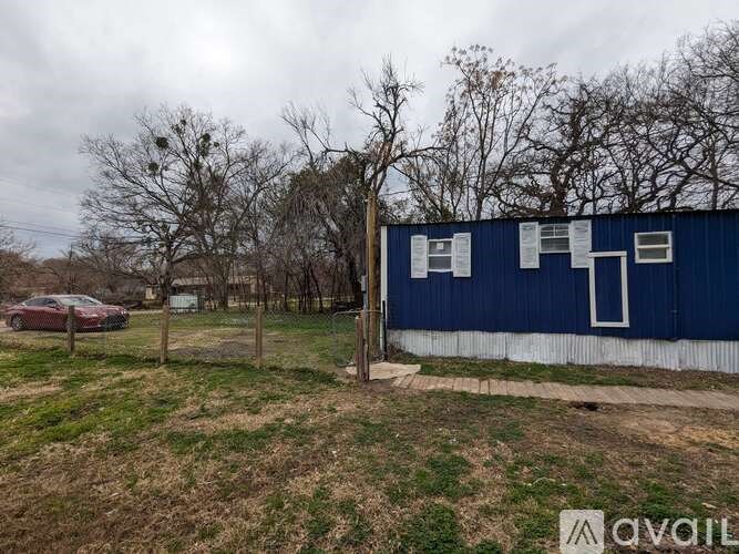 A blue building with a white door and windows is surrounded by a grassy field.