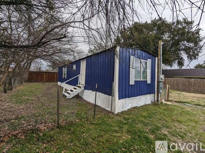 A blue and white mobile home sits in a grassy area with trees in the background.