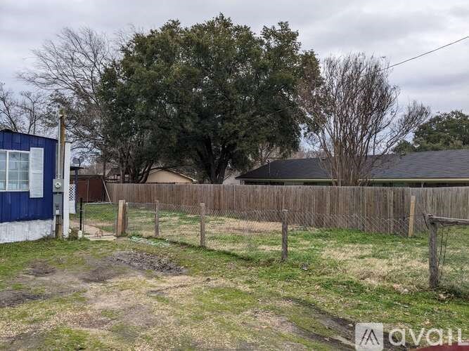 A blue and white building sits in a grassy field next to a wooden fence.