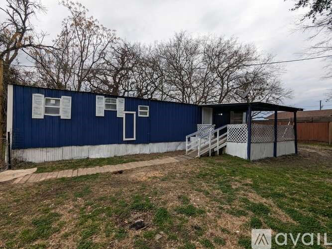 A blue building with white trim and a white door is surrounded by a grassy area and leafless trees.