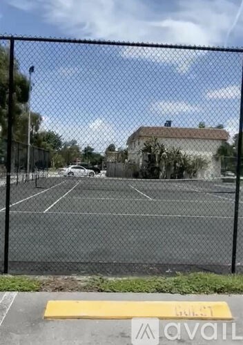A tennis court is enclosed by a fence and has a yellow sign on the ground.