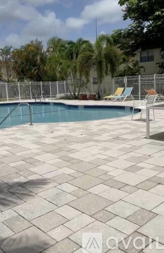A pool surrounded by a white fence and a tiled patio.