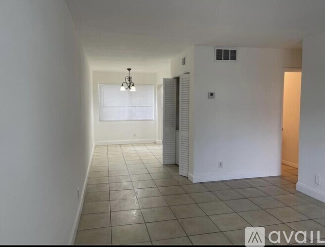 A long, narrow room with tiled flooring and a chandelier hanging from the ceiling.
