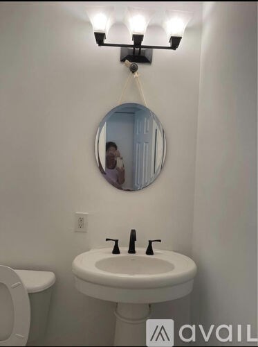 A bathroom with a white toilet and a white sink with a round mirror above it.