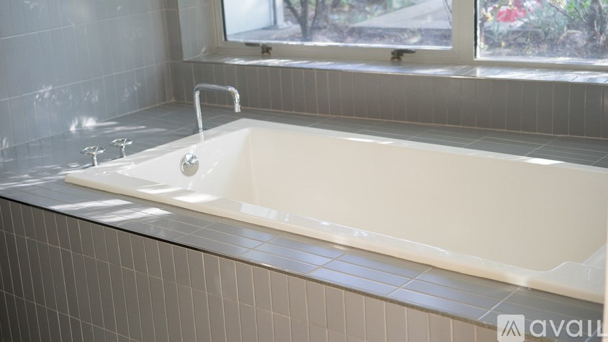 A white bathtub with a silver faucet is on a tiled bathroom counter.