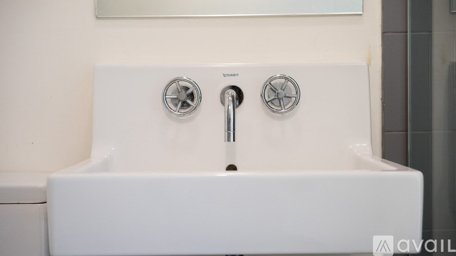 A white sink with two silver faucets and a silver handle.