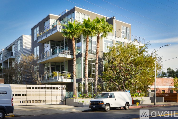 A white van is parked in front of a modern building with palm trees.