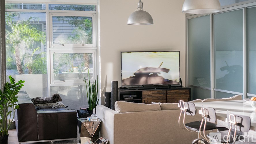 A living room with a brown couch, a white chair, a television, and a plant.